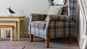 A plaid armchair with a pillow, a small table with a bird, and a carpeted floor.