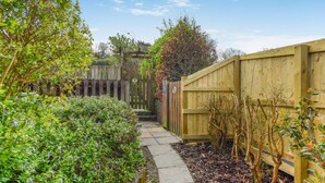 A garden pathway with a wooden fence, surrounded by greenery and a clear sky.