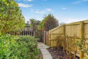 A garden pathway with a wooden fence, surrounded by greenery and a clear sky.