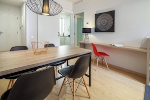 A modern dining area with a wooden table, black and red chairs, a geometric pendant light, and a wall-mounted artwork.
