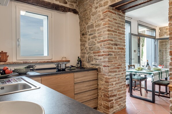 Une cuisine dotée d’une grande fenêtre, d’un mur en briques, de meubles en bois et d’un coin repas avec une table mise pour deux personnes.
