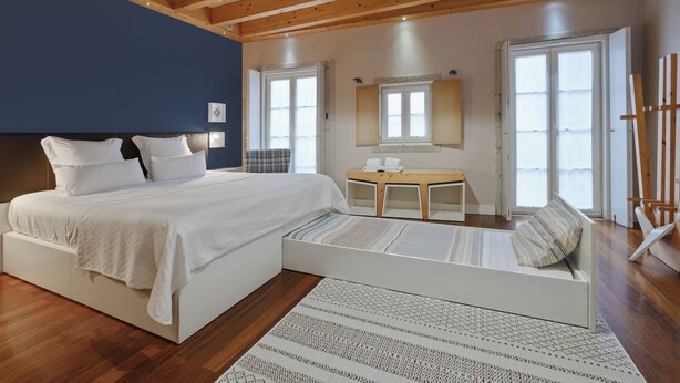 A modern bedroom with a large bed, a small table, and a painting on the wall. - Charming Porto Apartment with City and River Views (Porto)