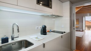 A modern kitchen with white cabinets, a stainless steel sink, a built-in microwave, and a kettle. - Charming Porto Apartment with City and River Views (Porto)