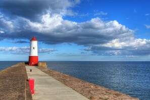 A lighthouse on a concrete pier with a view of the sea and a partly cloudy sky.