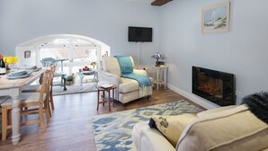Een woonkamer met een open haard, een eethoek met een tafel en stoelen, en een gezellige zithoek met een bank en fauteuils.