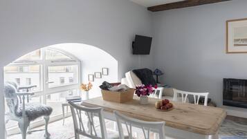 A dining area with a wooden table, white chairs, a vase with flowers, and a television mounted on the wall.
