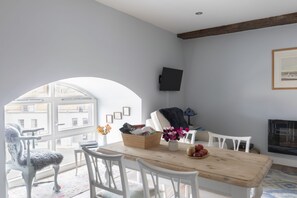 A dining area with a wooden table, white chairs, a vase with flowers, and a television mounted on the wall.