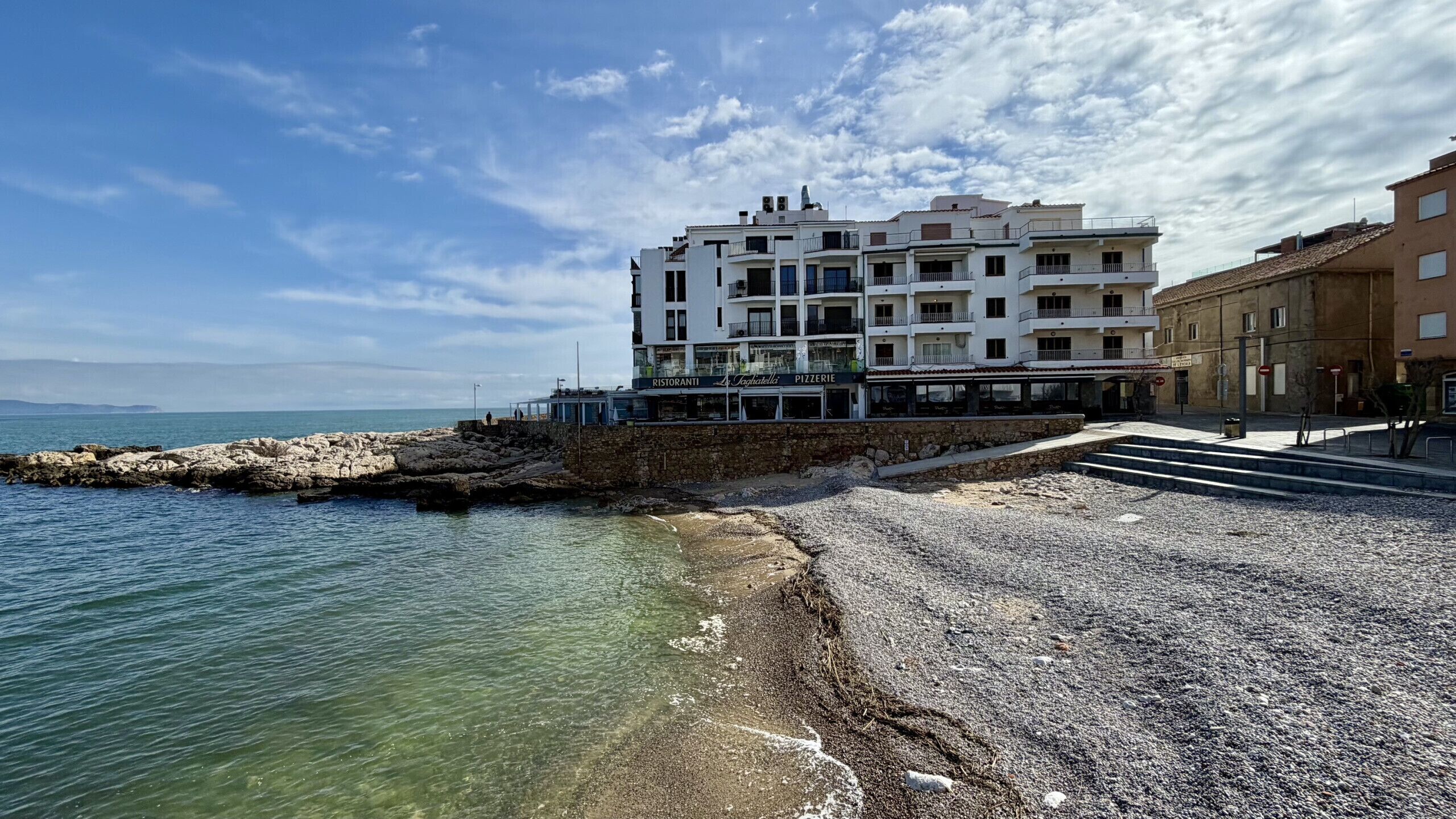 Un bâtiment situé sur la côte, doté de nombreux balcons, d’une promenade dallée et offrant une vue sur la mer.