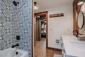 Bathroom features a sink and mirror, with a patterned wallpaper and a door leading to another room.