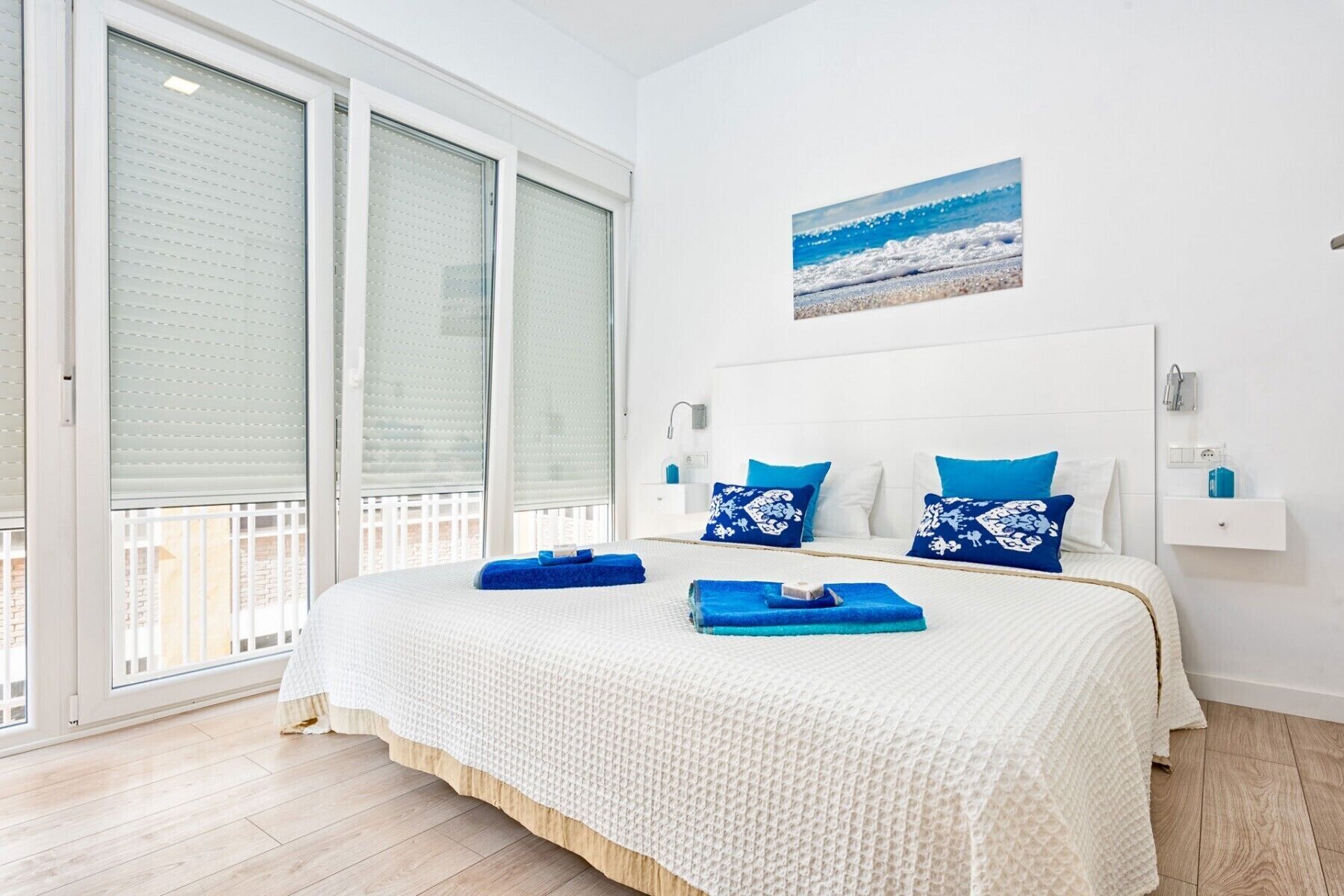 Une chambre avec un grand lit, des murs blancs et une vue sur la plage par la fenêtre.