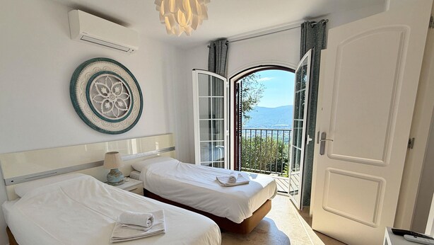 A hotel room with two beds, a large decorative plate on the wall, and a balcony with a view of the mountains.