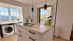 A modern kitchen with a built-in washing machine, a marble countertop, and a view of the outdoors.