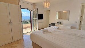 A bedroom with a large bed, a TV, a mirror, and a view of the outdoors.