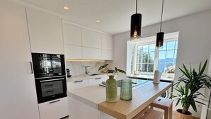 A modern kitchen with white cabinetry, a built-in oven, a large window, and a wooden island with bar stools.