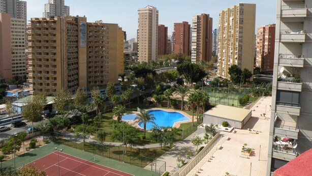 A high-rise residential building with multiple balconies, a swimming pool, and a tennis court. - GIJON (1 BEDROOM) BENIDORM (Benidorm)