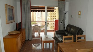 A living room with a sofa, a wooden table, a TV, and a balcony with curtains. - GIJON (1 BEDROOM) BENIDORM (Benidorm)