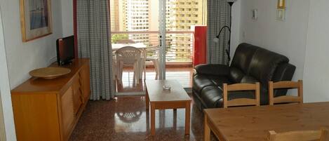 A living room with a sofa, a wooden table, a TV, and a balcony with curtains.