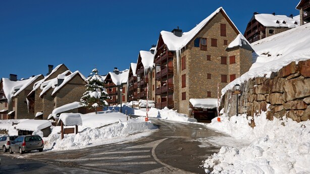 Ein schneebedecktes Bergresort mit Steingebäuden und Holzbalkonen.