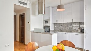 Eine moderne Küche mit weißen Schränken, einer Granitabdeckung und Edelstahlgeräten. Ein Esstisch mit Stühlen und eine Schale mit Obst sind ebenfalls vorhanden.