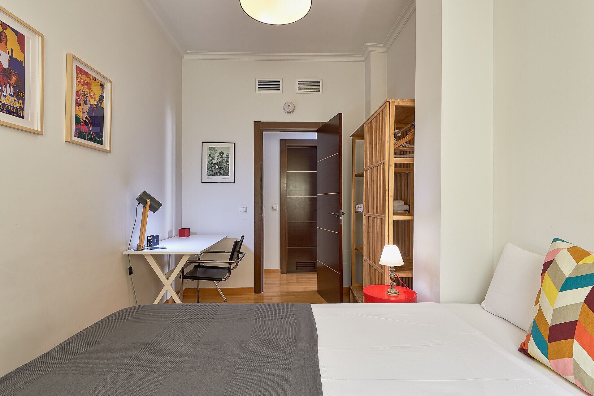 Une chambre à coucher comprenant un lit, un bureau avec une chaise, une armoire et deux tableaux encadrés accrochés au mur.