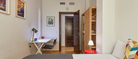 A bedroom with a bed, a desk with a chair, a wardrobe, and two framed pictures on the wall.