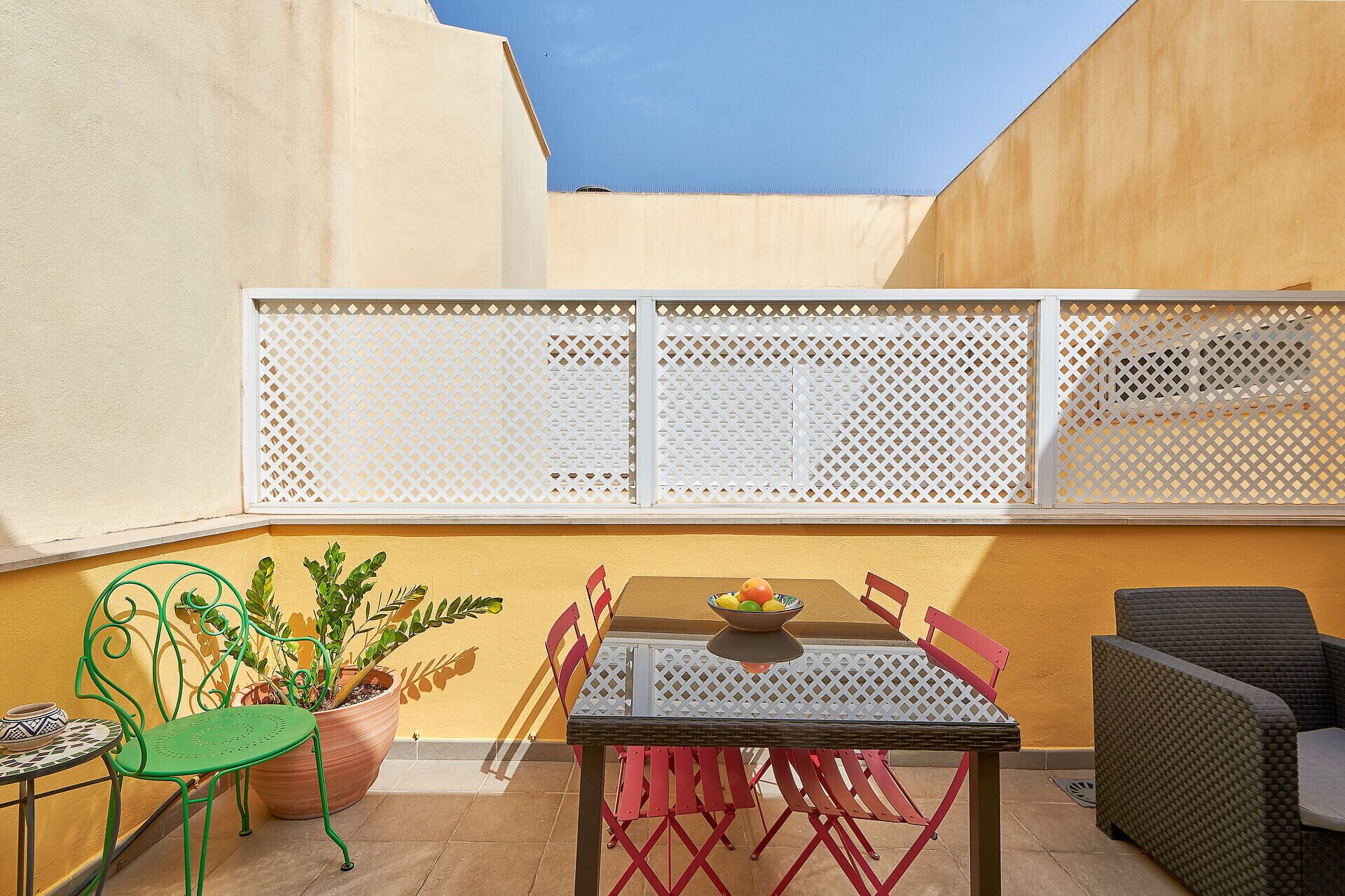 A patio with a table and chairs, a potted plant, and a wicker sofa.