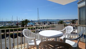 Un balcón con mesa y sillas, con vista a un puerto deportivo con barcos y un paisaje urbano distante.