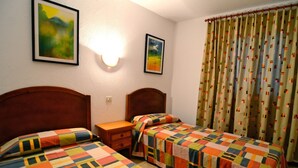 Una habitación de hotel con dos camas individuales, una mesita de noche, una lámpara y una ventana con cortinas.