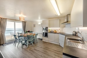 A modern kitchen with a dining area, large windows, and a view of the sea. - 4 Bed in Putsborough (oc-fl28) (Ilfracombe)