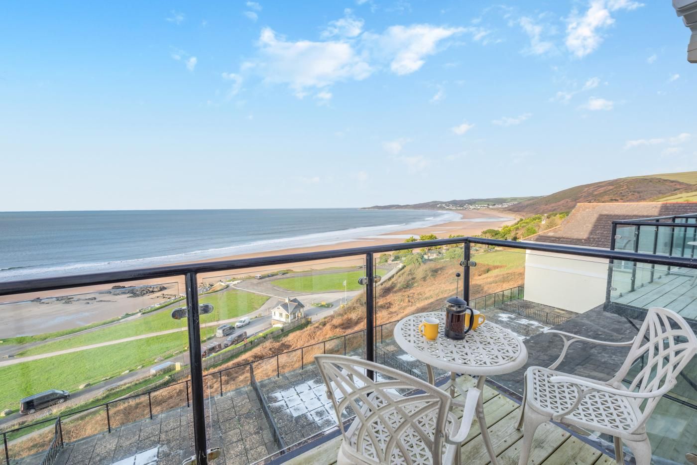 A balcony with a table and chairs overlooking a beach and ocean.