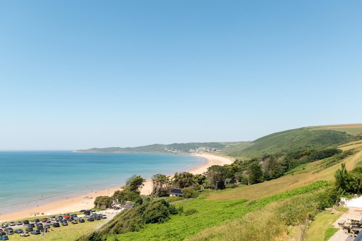 Un paysage côtier avec une plage, des collines verdoyantes et un ciel dégagé.