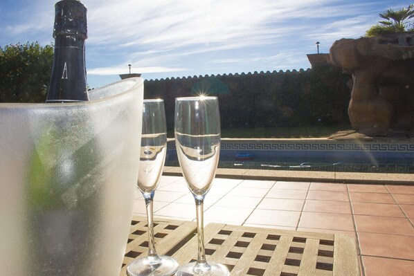 A poolside setting with two champagne flutes on a tiled table, a large ice bucket, and a stone structure in the background.