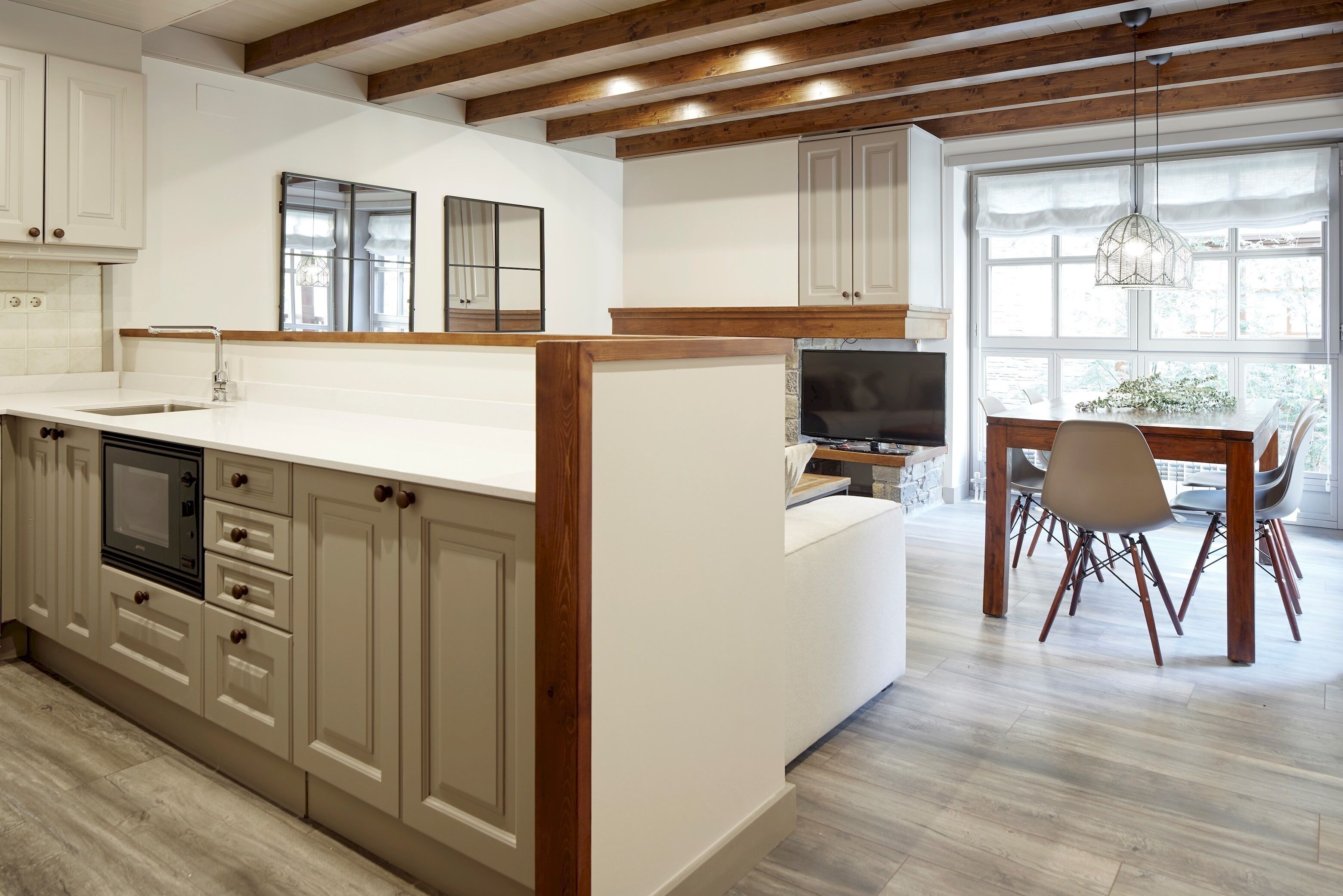 A modern kitchen with wooden beams, a large island, and a dining area with a TV.