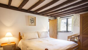 Quarto com cama de madeira, mesa de cabeceira com abajur, janela com cortinas e porta de madeira.