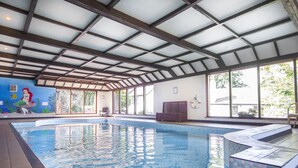 Piscina interna com água azul cristalina, um mural na parede e grandes janelas que permitem a entrada de luz natural.