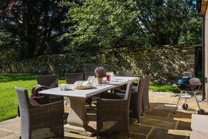 An outdoor patio with a stone wall, wicker chairs, a table set with cups and a pitcher, and a grill.
