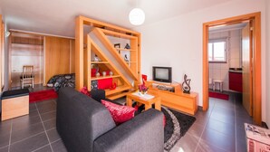 Moderni olohuone, jossa on sohva, sohvapöytä, televisio ja puinen kirjahylly.