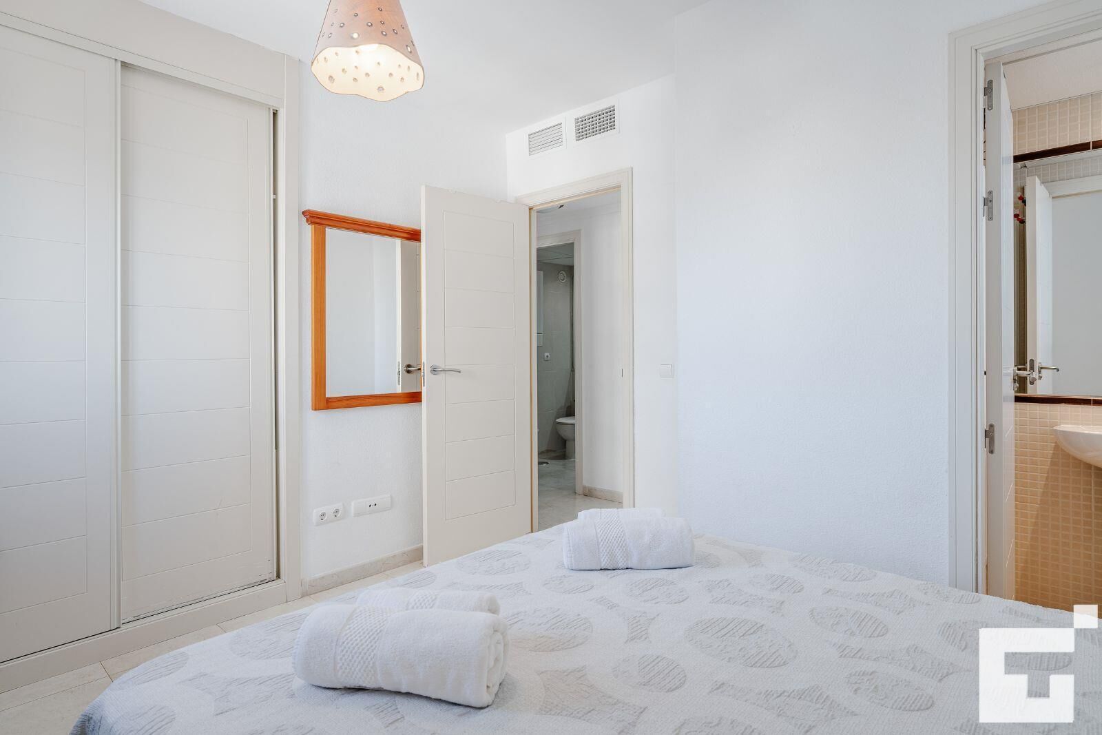Een slaapkamer met een bed, twee witte handdoeken, een hanglamp en een badkamer die door een open deur zichtbaar is.