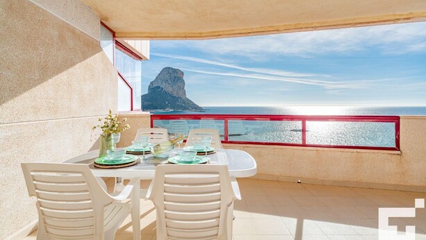 Un coin repas avec une table dressée pour deux personnes, offrant une vue sur la côte et mettant en valeur une formation rocheuse imposante.