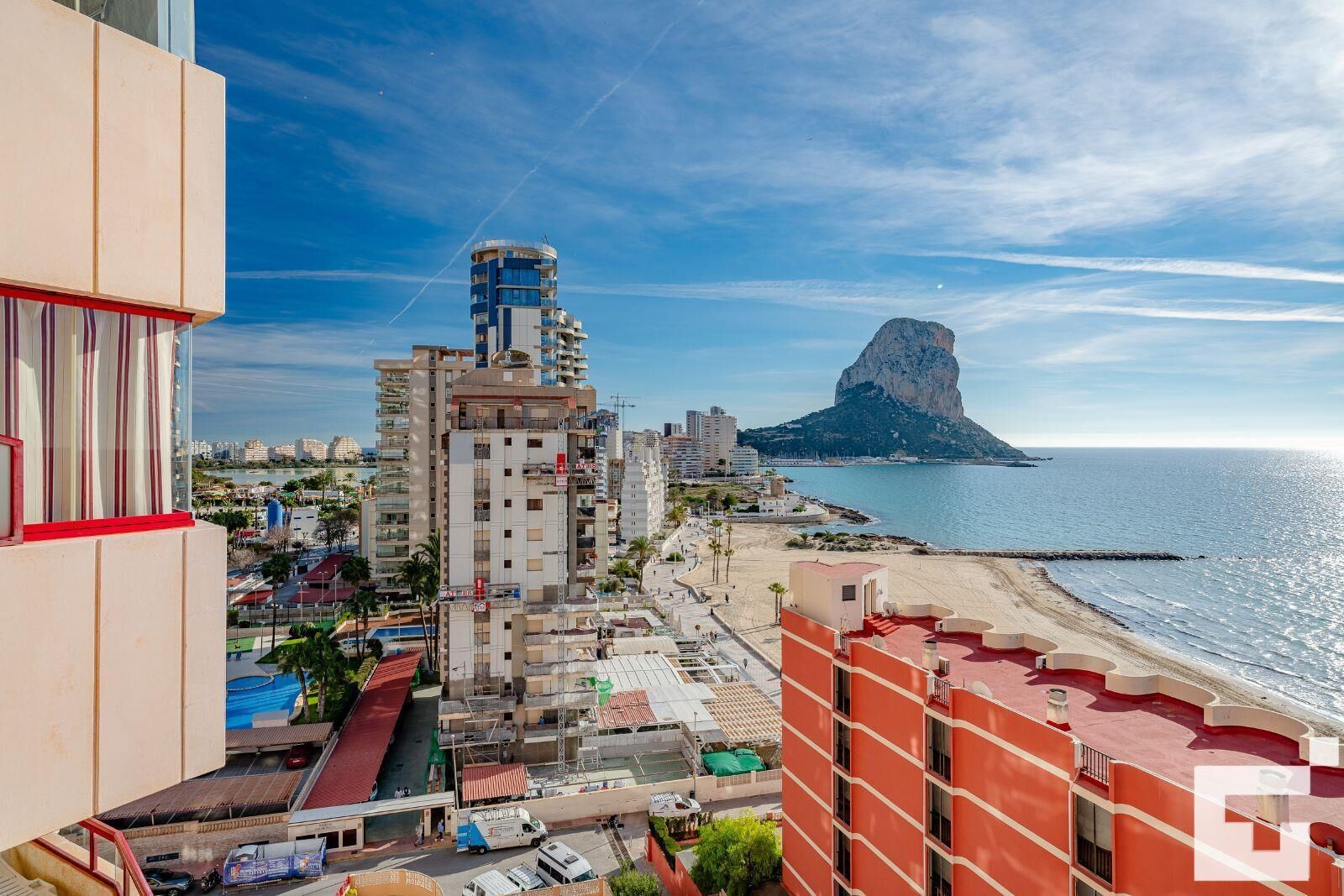 A coastal cityscape with a prominent mountain in the background, a beach, and various buildings including a tall structure with a blue top.