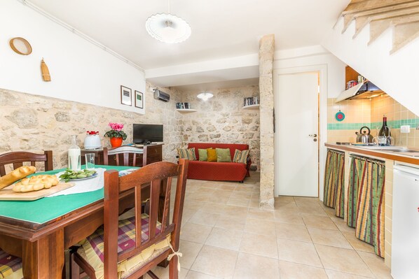 A cozy dining area with a wooden table set for a meal, a red sofa in the background, and a kitchen with tiled backsplash and wooden cabinets.
