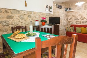 A dining area with a green tablecloth, wooden chairs, a cutting board with bread, a vase with flowers, and a television on a stone wall. - Rooftop house in the center, 2/4 guests, free illimited WIFI, free parking (Scicli)