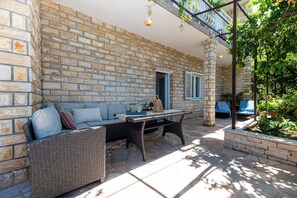 Un patio con paredes de piedra, un sofá de mimbre, una mesa y una silla azul.