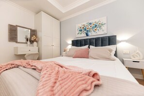 Un dormitorio con cama, mesitas de noche, cómoda, espejo y un cuadro en la pared.