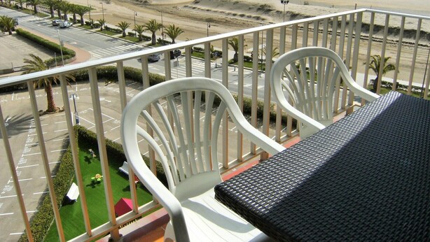 A balcony with white chairs and a black table overlooking a beach and a parking lot. - ROCAMAURA I B 6-1 (Estartit)