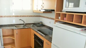 A kitchen with wooden cabinets, a stainless steel sink, a microwave, and a dishwasher. - ROCAMAURA I B 6-1 (Estartit)