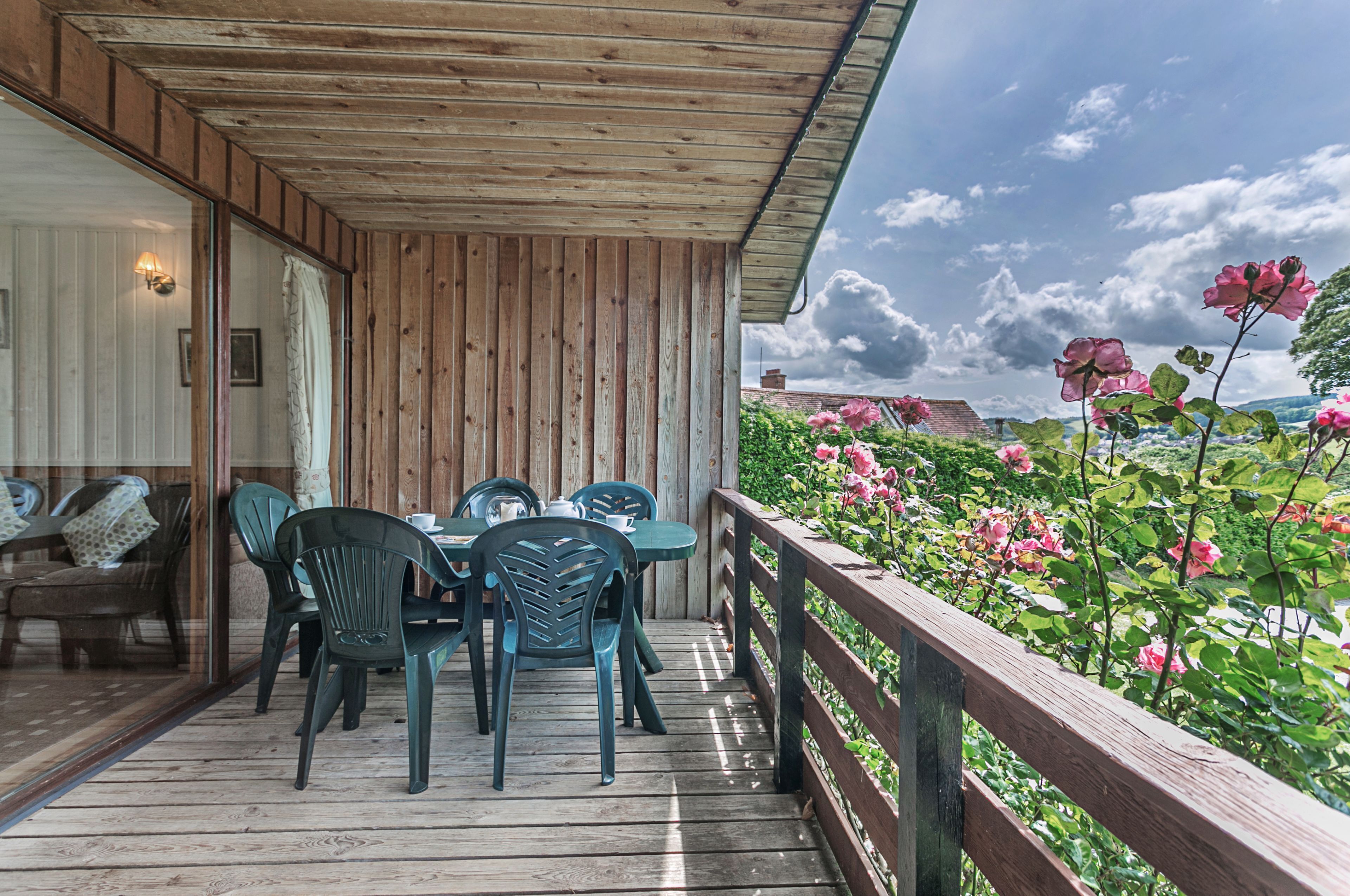 Une terrasse en bois avec une table et des chaises, donnant sur un jardin où poussent des fleurs roses.