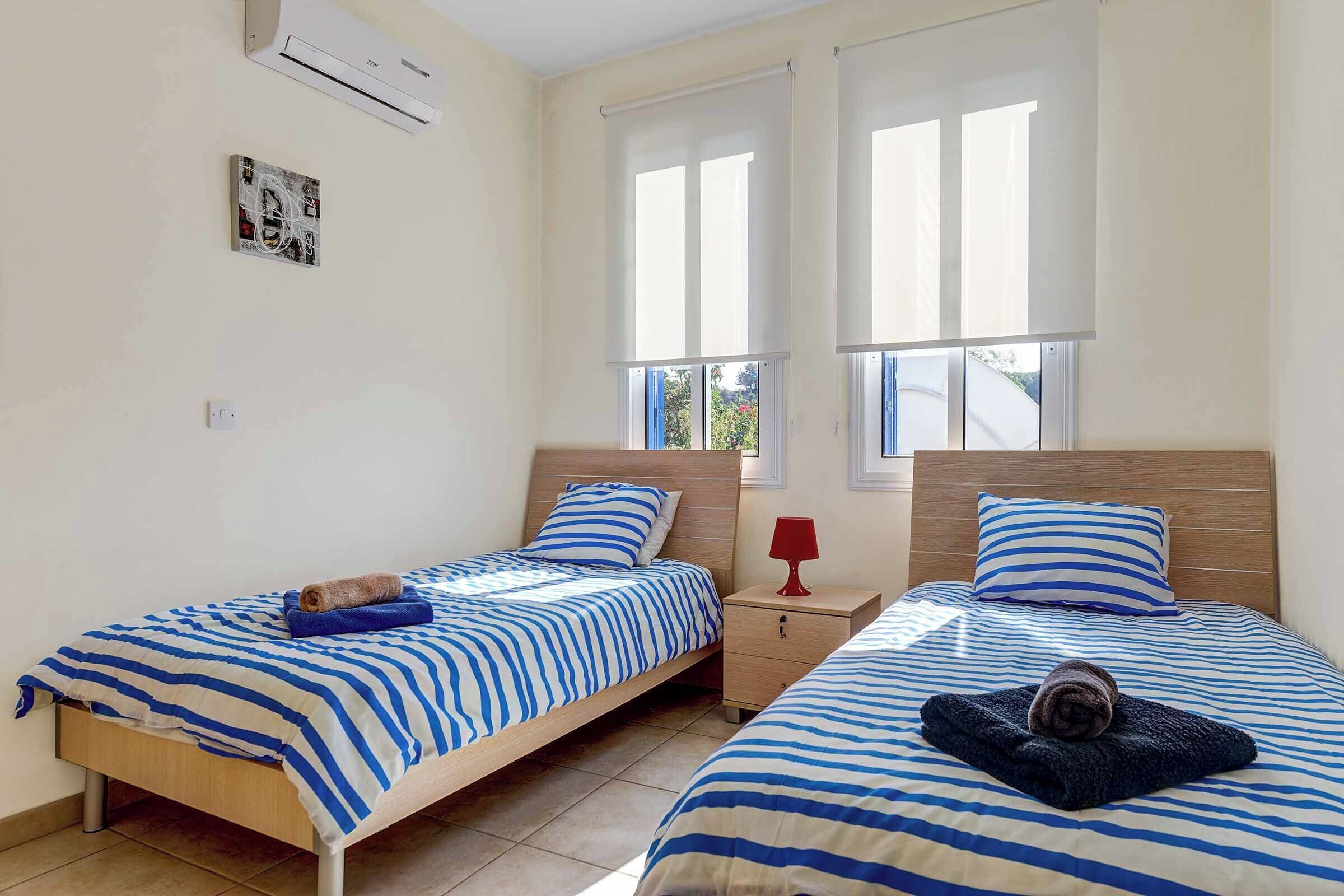 A bedroom with two beds, a nightstand, a red lamp, and an air conditioner.