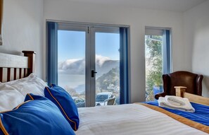 A hotel room with a bed, a chair, and a view of a mountain and a car through the window.
