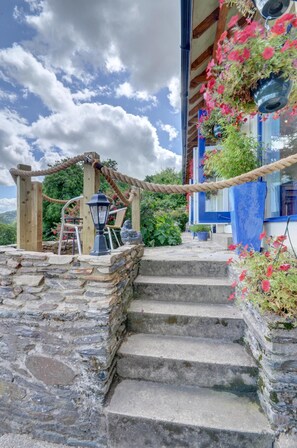 A stone staircase leading to a wooden deck with a rope archway, a lantern, and potted plants.